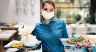 Beautiful young waitress with face protective mask working in exclusive restaurant. Coronavirus or Covid-19 concept.
